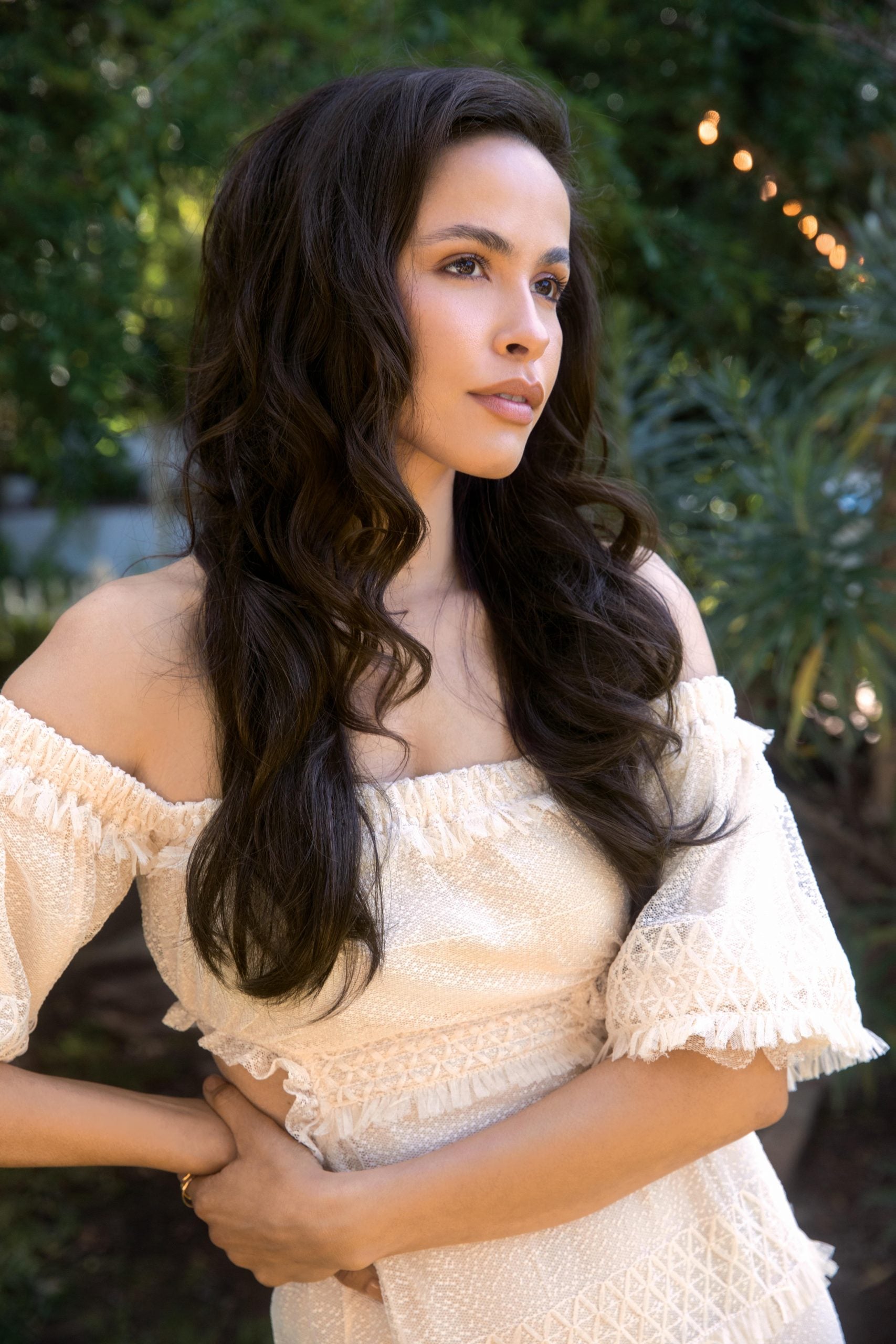 layered dark brown wig for women long wavy natural look on model outdoors wearing off shoulder cream dress