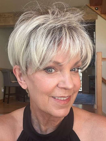 Smiling mature woman wearing a short blonde synthetic wig styled in a layered pixie cut with soft bangs