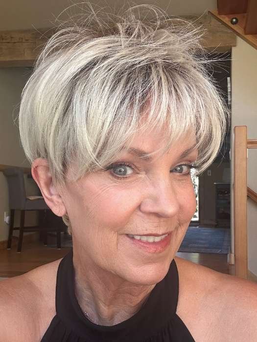 Smiling mature woman wearing a short blonde synthetic wig styled in a layered pixie cut with soft bangs