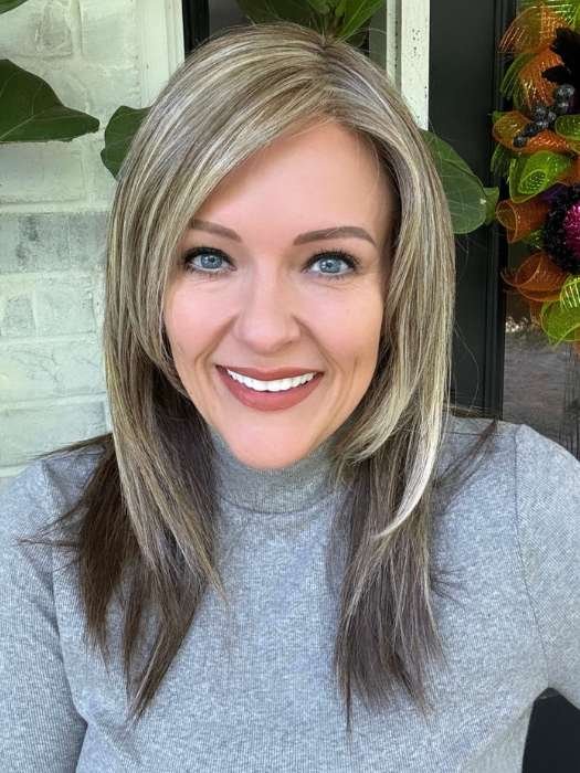 Smiling woman wearing a natural looking blonde wig with layered shoulder length cut and face framing highlights