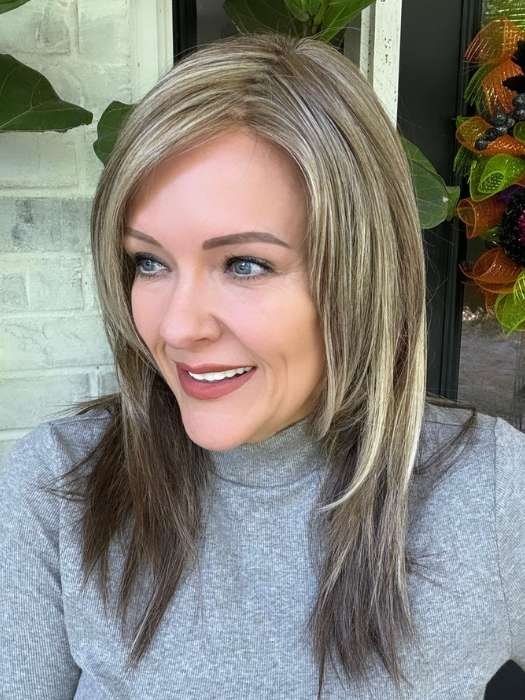Woman wearing natural looking blonde wig with brown lowlights mid length layered straight hair and side part